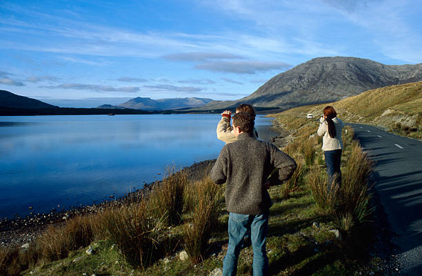 tourists looking at panoramic view A small group of people is standing on the road side to gaze at the astonishing scenery of Connemara in Ireland. A bus tour is leading the visitors to the most beautiful spots in Connemara and every now and then the driver stops for a couple of photos. The sun is standing low and sky almost clear. connemara stock pictures, royalty-free photos & images