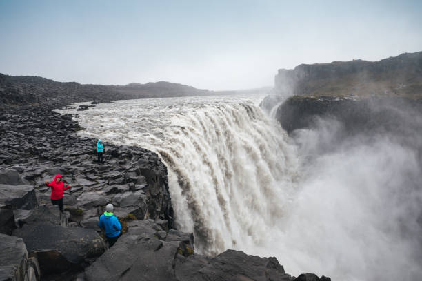 Tourists Photographing Dettifoss In Iceland Dettifoss, Iceland - September 8, 2017: Tourists in colorful clothes taking photos of Dettifoss waterfall in Vatnajökull National Park in Northeast Iceland. Famous waterfall is one of the most powerful waterfalls in Europe. iceland dettifoss stock pictures, royalty-free photos & images