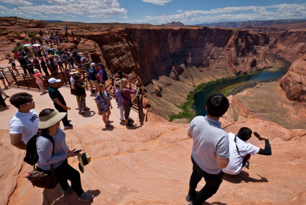 Tourists Taking Pictures at Horseshoe Bend Page, Arizona, USA - May 31, 2019: The Colorado River provides some incredible natural vistas along its length. One of the more unusual vistas is at Horseshoe Bend. The name was inspired by its unusual shape, a horseshoe-shaped meander of the river. Horseshoe Bend, located about four miles southwest of Page, Arizona, USA within the Glen Canyon National Recreation Area has become a very popular tourist attraction. In this picture, the tourists stand on the steep cliff overlooking the river. jeff goulden people stock pictures, royalty-free photos & images