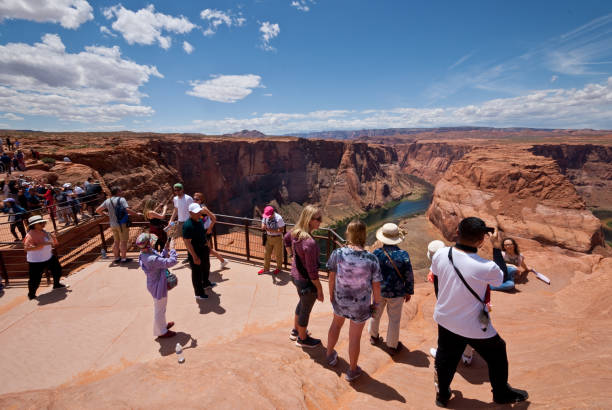 Tourists Taking Pictures at Horseshoe Bend Page, Arizona, USA - May 31, 2019: The Colorado River provides some incredible natural vistas along its length. One of the more unusual vistas is at Horseshoe Bend. The name was inspired by its unusual shape, a horseshoe-shaped meander of the river. Horseshoe Bend, located about four miles southwest of Page, Arizona, USA within the Glen Canyon National Recreation Area has become a very popular tourist attraction. In this picture, the tourists stand on the steep cliff overlooking the river. jeff goulden people stock pictures, royalty-free photos & images