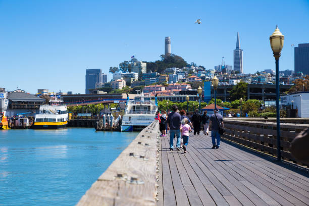 tourists walking on the deck at Fisherman's Wharf with Coit Tower in the background stock photo