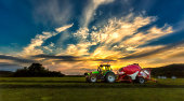 Green tractor with red silage packer in sunset light