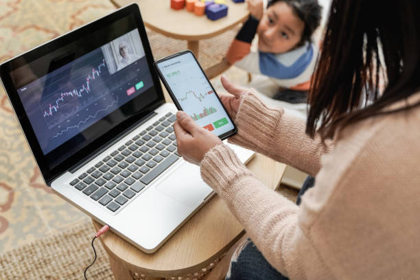 Trader mother studying stock market on streaming lesson with her child at home - Blockchain analysis concept - Focus on left hand holding mobile phone stock photo