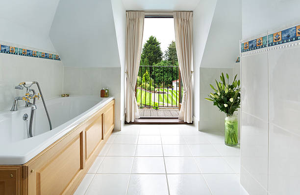 Traditional Bathroom and garden view a traditional bathroom with a lovely view through the balcony doors over a lovely mature garden. An enamel bath with wood side panels sits to the left, with traditional chrome and gold plated taps. The floor and walls are tiled in light grey porcelain tiles. porcelain stock pictures, royalty-free photos & images