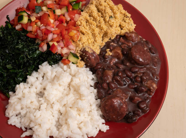 traditional Brazilian dish of feijoada consisting of five ingredients - feijoada, farofa, english sauce, rice and covey on red plate stock photo