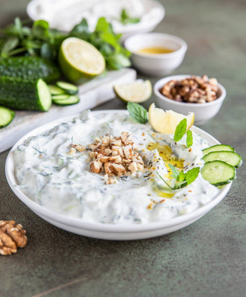 Traditional bulgarian cold summer soup tarator with ingredients on green background. Bulgarian soup with grated cucumbers, yogurt and walnuts. stock photo