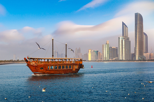 Dubai, UAE 11. 10. 2018 : Famous traditional wooden old dhow cruise tour in the marina with tourist on the board and modern skyscrapers in the backgound