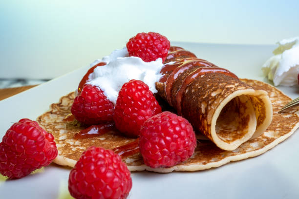 Traditional Finnish cuisine: Finnish pancakes on a plate with whipped cream and raspberry jam on the side stock photo