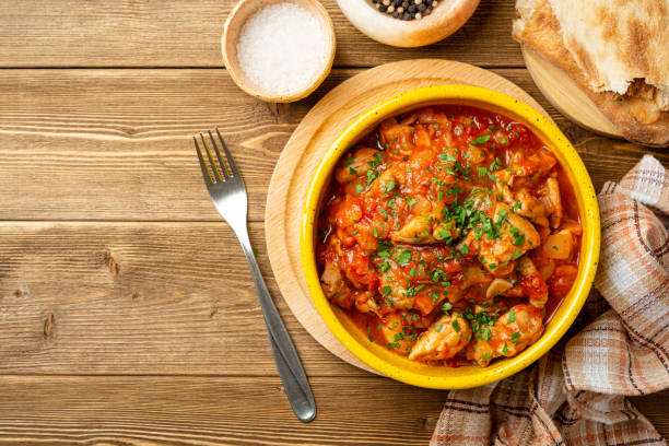 Traditional georgian dish Chakhokhbili. Chicken stew with tomatoes in ceramic bowl on wooden background stock photo