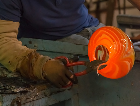 traditional glassblowing worker cutting liquid glass