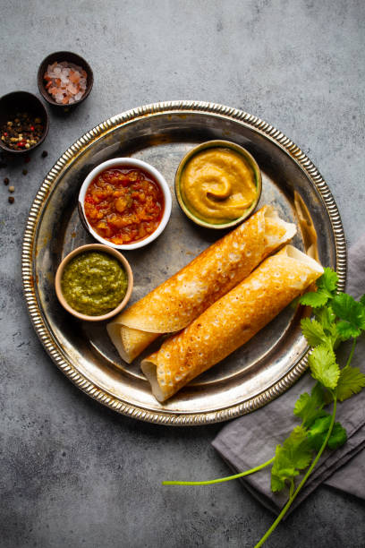 Traditional Indian rice pancakes Dosa with different dips chutney and seasonings on rustic metal plate on stone background table. Quick meal or vegetarian snack of South India, top view Traditional Indian rice pancakes Dosa with different dips chutney and seasonings on rustic metal plate on stone background table. Quick meal or vegetarian snack of South India, top view thosai stock pictures, royalty-free photos & images