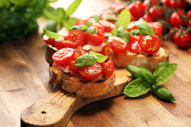Traditional italian antipasto bruschetta appetizer with cherry tomatoes, cream cheese, basil leaves and balsamic vinegar on cutting board. Antipasti stock photo
