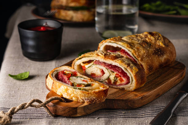 Traditional Italian Stromboli stuffed with cheese, salami, red pepper and spinach. Photo in a dark style. stock photo