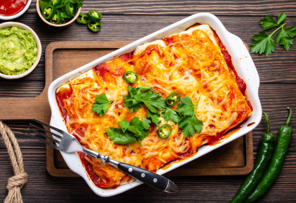 Traditional Mexican enchiladas Traditional Mexican dish enchiladas with meat, chili red sauce and cheese in white casserole dish over rustic wooden background, served with guacamole and tomato dips. Close up, top view casserole stock pictures, royalty-free photos & images