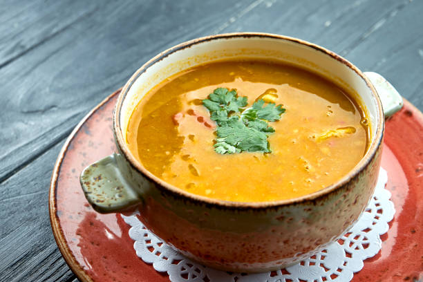 Traditional Moroccan soup - Harira, yellow lentil soup with cilantro in a red plate on a black wood background. Diet soup stock photo