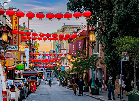 San Francisco, USA - December 18, 2021: Traditional shops, lanterns and people in the street in Chinatown near Downtown with a fiery sunset