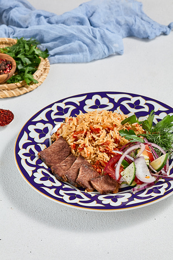 Traditional uzbek food - plov with beef. Eastern cuisine - pilaf with rice, meat and spices. Plov with beef on traditional uzbek plate. Composition of oriental ceramic plate with pilaf