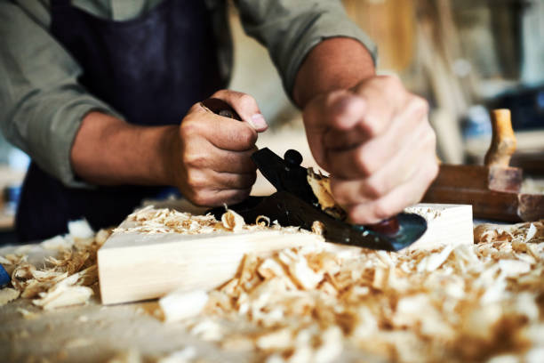 Traditional Woodworking Craft Closeup portrait of strong male hands shaving piece of wood with plane tool in carpenters workshop making furniture carpenter photos stock pictures, royalty-free photos & images