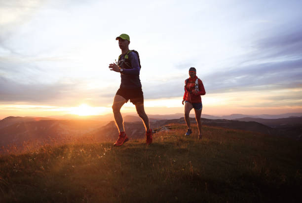 Trail running couple Two athletes trail running in the hills during sunset. Shallow D.O.F. and with motion blur. cross country running stock pictures, royalty-free photos & images