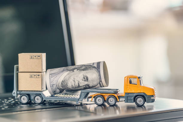 Trailer truck transports or delivers US USD 100 dollar bill, boxes of goods on a laptop computer stock photo