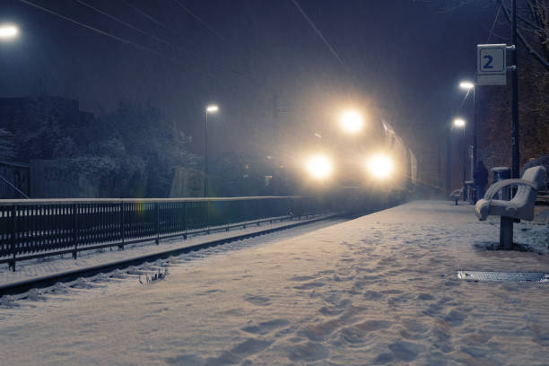 Train with strong headlights arriving at station on a snowy night stock photo