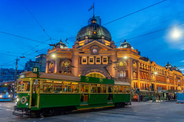 Tram passing Flinders Street Station at dusk A tram passes Flinders Street Station at dusk. international landmark stock pictures, royalty-free photos & images
