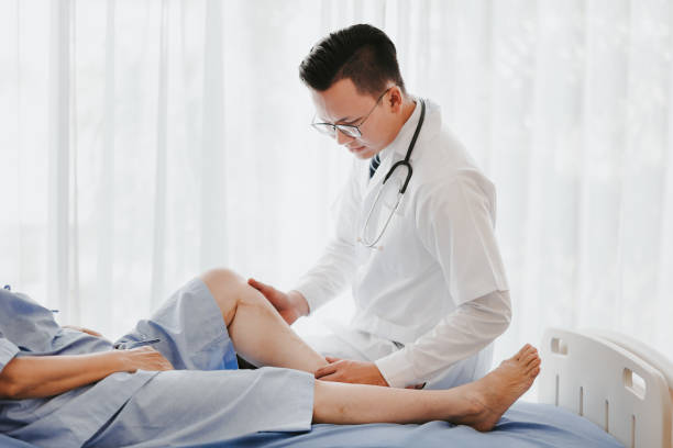 traumatologist doctor examining his patient knee Shot of a traumatologist doctor examining his patient knee on the bed in hospital orthopedics stock pictures, royalty-free photos & images