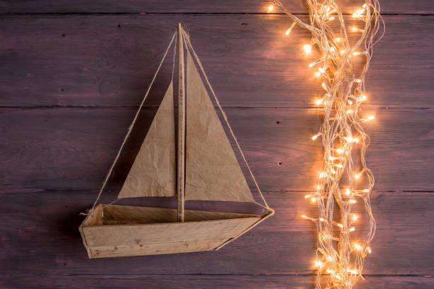 Travel and adventure creative concept - toy boat on a wooden background. Christmas lights as a sea waves stock photo