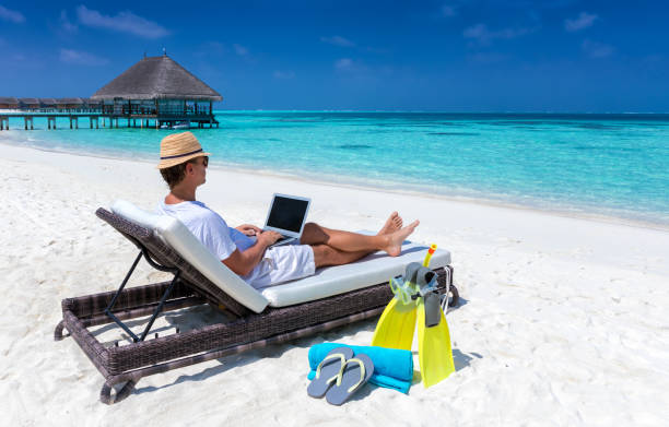 旅行者男は彼のラップトップの作品と熱帯のビーチに座ってください。 - 島で働く ストックフォトと画像