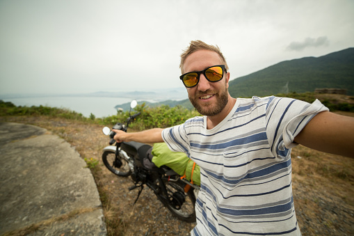 Young man traveling with his motorbike on the Hai Van pass in Vietnam taking a selfie.