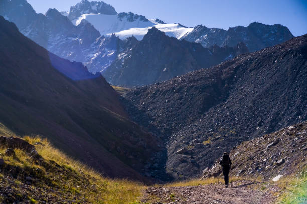 Traveler walks in the mountains on a sunny day. High mountains with snowy peaks in the national park in the sunshine, the traveler goes through a difficult route, is engaged in hiking and mountaineering. tien shan mountains stock pictures, royalty-free photos & images