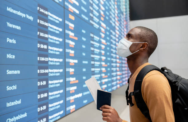 Traveler wearing a facemask at the airport and looking at the flight schedule Portrait of a black male traveler wearing a facemask at the airport and looking at the flight schedule - travel concepts airport terminal photos stock pictures, royalty-free photos & images