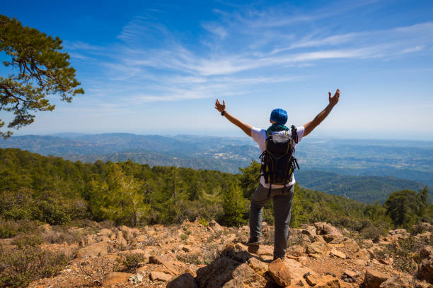 Traveler with open arms stands on the cliff, among green hills stock photo