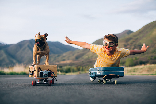 A young boy and his French Bulldog are ready to travel the world. They have put their suitcases on skateboards and are wearing flight goggles, ready to fly to new places and heights. Image taken in Utah, USA.