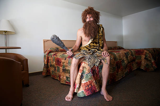 Traveling Caveman Sitting on Old Fashioned Motel Room Bed stock photo