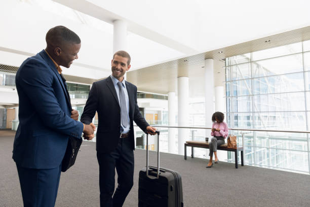 Travelling businessmen shaking hands Front view of a young African American and a young Caucasian businessman shaking hands while travelling with luggage. Modern corporate start up new business concept with entrepreneur working hard business travel photos stock pictures, royalty-free photos & images