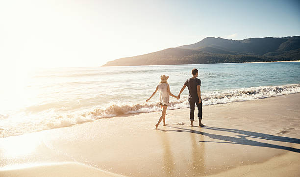 Treating themselves to a beachside vacation Shot of a young couple going for a stroll along the beach tasmania photos stock pictures, royalty-free photos & images