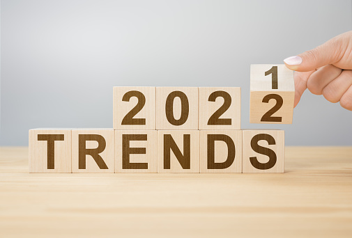 Trends 2022 blocks. 2022 trends new year symbol. woman turns a wooden cube and changes words Trends 2021 to Trends 2022. Flipping of wooden cube block. gray background, copy space.