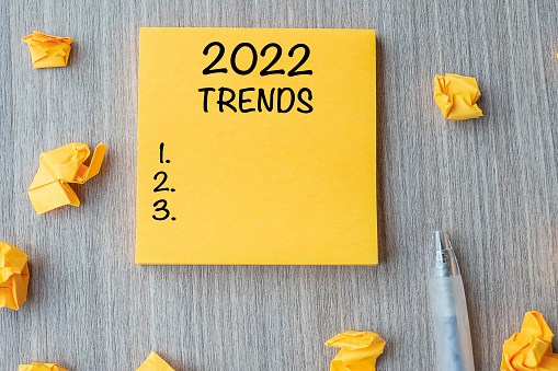 2022 Trends word on yellow note with pen and crumbled paper on wooden table background. New Year New Start, Resolutions, Strategy and Goal concept