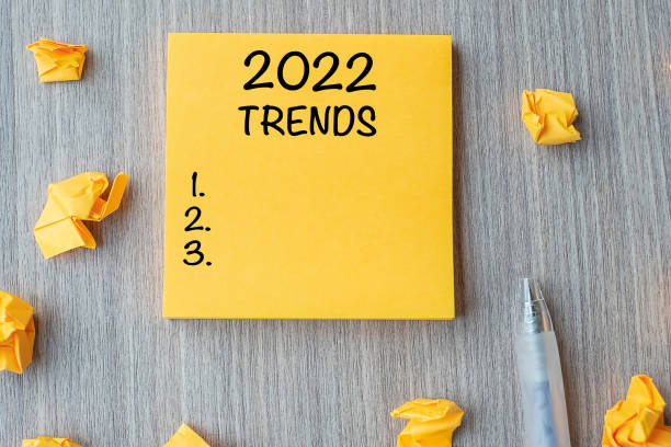 2022 Trends word on yellow note with pen and crumbled paper on wooden table background. New Year New Start, Resolutions, Strategy and Goal concept stock photo