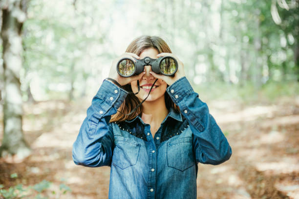 Trendy young woman using binoculars in the woods stock photo