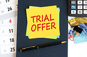 Trial offer, text on yellow paper square shape on a blue background. Notepad, calculator, credit cards, pen, stationery on the desktop. Business, financial and education concept. Selective focus.