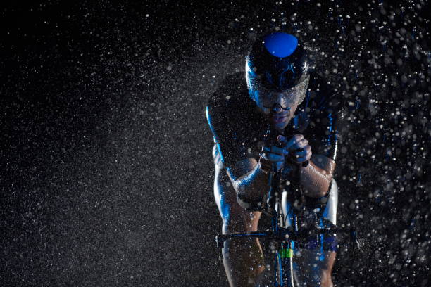 triathlon athlete riding bike fast on rainy night stock photo