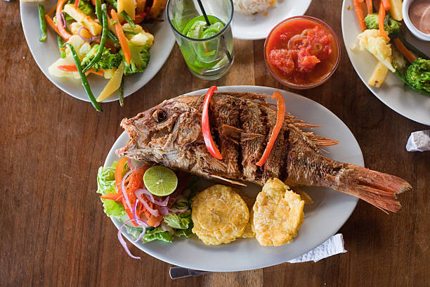 Tropical Dinner An entire deep fried fish sits on a plate on a full table. Typical food in Nicaragua, with tostones and salad. fried fish stock pictures, royalty-free photos & images