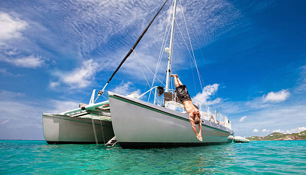 Tropical Vacation: Man Diving Off Sailboat A mature man enjoys his vacation by diving off of the deck of a catamaran sail boat into the turquoise waters of the Caribbean on a beautiful day. catamaran stock pictures, royalty-free photos & images