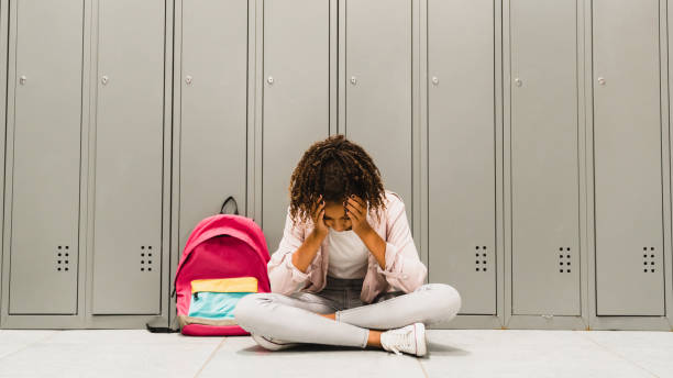 Troubles at school. Lonely sad african-american schoolgirl crying at school hall. Social exclusion problem. Bullying at school concept. Racism problem.Puberty difficult age stock photo