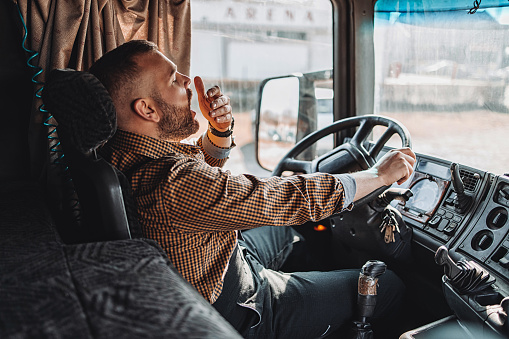Young handsome bearded man driving his truck. View inside of cabin. He is tired, sleepy and yawns.