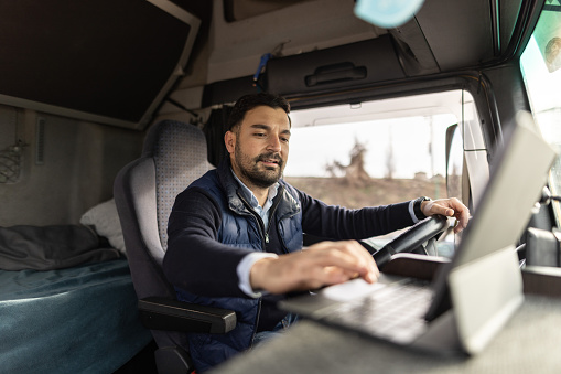 Young truck driver typing destination on tablet while sitting in truck cabin