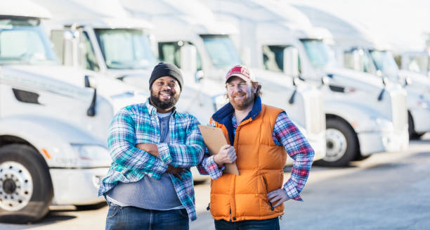Truck drivers with fleet of semi-trucks Two multi-ethnic men standing in front of a fleet of semi-trucks or tractor-trailers. The one holding the clipboard is a mature man in his 40s. The other is an African-American man in his 30s. truck driver stock pictures, royalty-free photos & images
