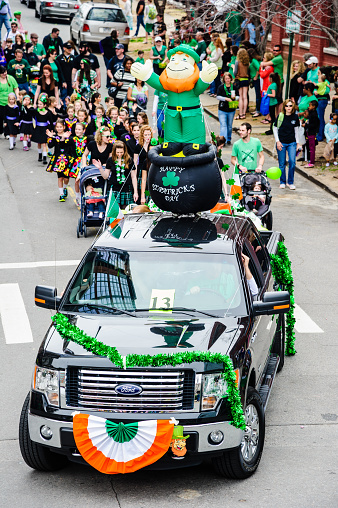 Little Rock, Arkansas, USA - March 15, 2014: A truck is decorated with banners and an inflatable figure of a leprechan while participating in a St. Patrick's day parade. Children from an irish dance group follow behind, and spectators watch from the side.